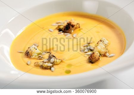 Pumpkin soup in white bowl. Served main course close up. Vegetable cream soup decorated with seeds. Restaurant food portion, main course. Vegetarian supper. Dinner, gourmet meal in plate