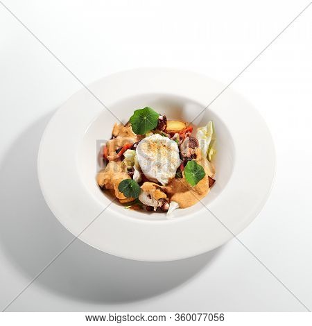 Salad in white bowl. Sliced octopus and fried potato. Served cut ingredients with mayonnaise, tomato spicy ajika and smoked pepper homemade sauce. Restaurant food portion in plate close up