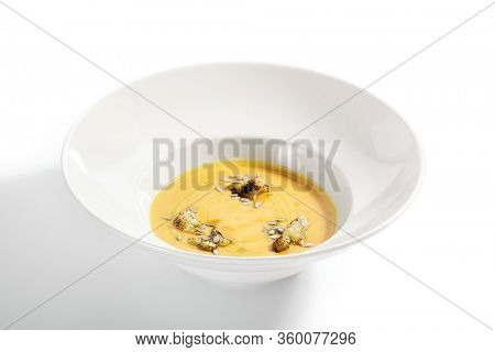 Pumpkin soup in white bowl. Served main course close up. Vegetable cream soup decorated with seeds. Restaurant food portion, main course. Vegetarian supper. Dinner, gourmet meal in plate