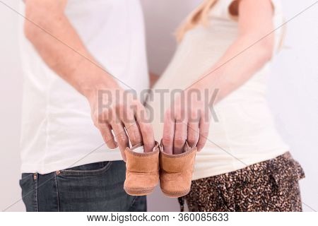Stock Photo Of A Pregnant Couple Holding A Pair Of Little Shoes. Photo Without Visible Faces.