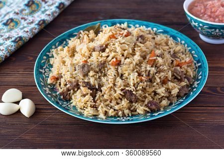National Cuisine - Uzbek Pilaf With Meat In A Plate With A Traditional Pattern, On A Dark Wooden Tab