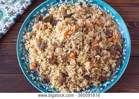 National Cuisine - Uzbek Pilaf With Meat In A Plate With A Traditional Pattern, On A Dark Wooden Tab