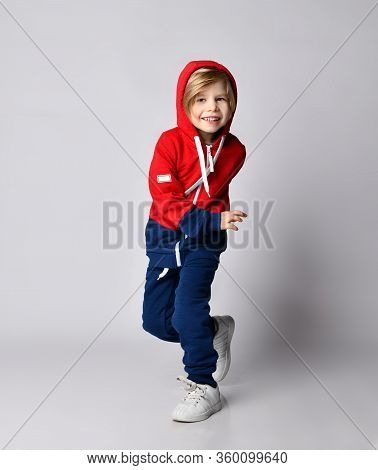 Full Growth Portrait Of Cheerful Blond Kid Boy In Blue And Red Sport Suit Hoodie And Pants With His 