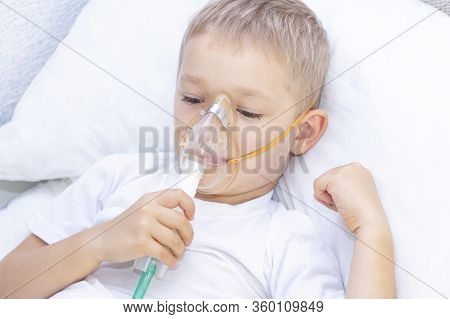 Boy With An Inhaler Mask - Respiratory Problems In Asthma. A Boy With An Inhaler Mask Lies In Bed An