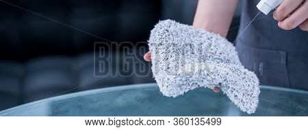 Young Woman Maid In Apron Is Cleaning, Wiping Down Office Glass Table Surface With Spray Bottle Clea