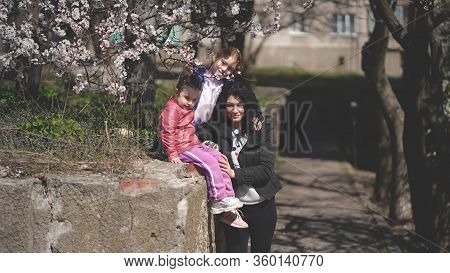Mom With Two Cute Daughters In A Park Near A Flowering Tree In Spring. Concept Of Happy Family And S