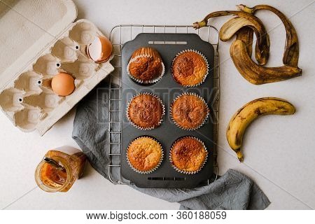 Homemade Banana And Honey Muffins In Mufin Tray Cooling On Rack, Eggs, Banana Peel, Honey On Kitchen