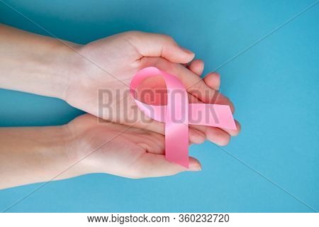 Pink Ribbon On A Womans Handon And Blue Background. Breast Cancer Concept Symbolic Tape