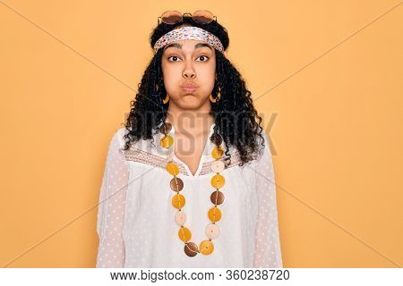 Young african american curly hippie woman wearing sunglasses and vintage accessories puffing cheeks with funny face. Mouth inflated with air, crazy expression.