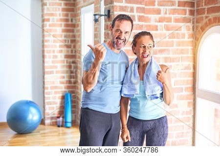 Middle age sporty couple standing before do exercise at gym smiling with happy face looking and pointing to the side with thumb up.