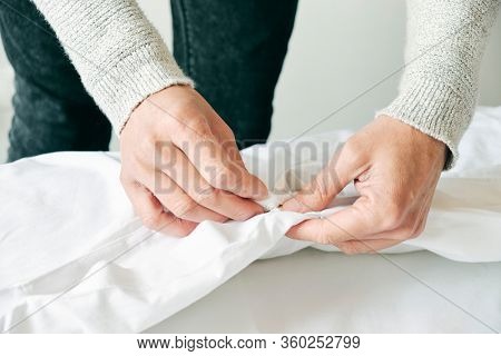 closeup of a young caucasian man inserting a duvet into a white duvet cover as he is making the bed