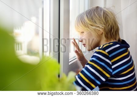 Sed Little Boy Looking Into Window During Coronavirus Pandemic. Child Boring Without Communication A