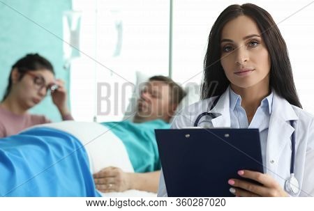 Doctor With Folder Is Standing In Palette Sick Man. Patient Are Monitored By Staff On Duty. Remote M