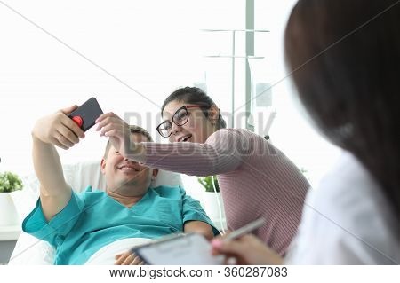 Husband And Wife Take Selfie In Hospital Bed. Doctor Motivates Patient. Single Room Is Equipped With