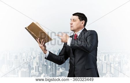 Senior Businessman Finger Pointing Into Open Old Book. Portrait Of Adult Man In Business Suit And Ti