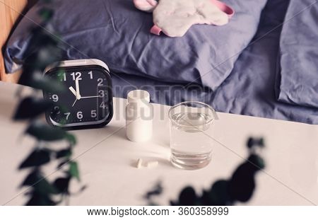 Healthy Sleep Concept. Medical Capsules And Glass Of Water On Bedside Table. Melatonin And Circadian