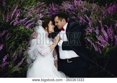 Couple At Sunset In A Wedding Dress Lie On The Grass With Lipin Flowers,festive Spring Wedding Photo