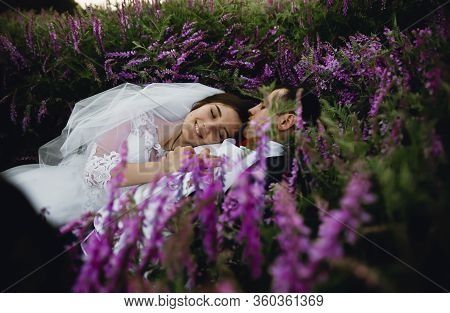 Couple At Sunset In A Wedding Dress Lie On The Grass With Lipin Flowers,festive Spring Wedding Photo