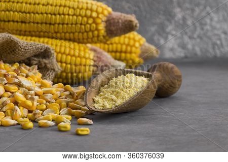 Corn flour in wooden bowl and spoon with dried corn groats, kernels on rustic table. corn ingredient