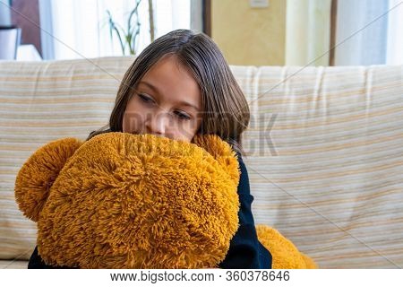 Beautiful Little Girl In A Black Jacket Playing With Her Brown Teddy Bear Who Has Put A Mask To Prot