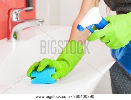 Woman cleaning sink and faucet in bathroom at home