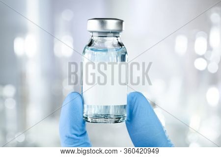 Healthcare concept with a hand in blue medical gloves holding a vaccine vial with blue liquid and black white label