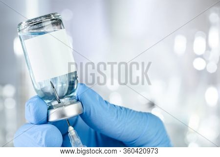 Healthcare concept with a hand in blue medical gloves holding a vaccine vial with blue liquid and black white label