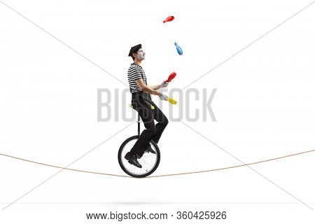 Full length profile shot of a mime riding a mono-cycle on a rope and juggling isolated on white background