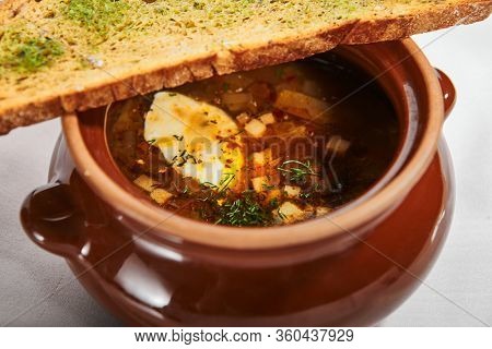 Oven baked meat soup with artichokes in pot. Delicious hot pottage with fresh bread and greenery. Traditional cuisine, restaurant dish, dinner food. Aromatic goulash on white napkin