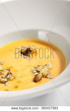 Pumpkin soup in white bowl. Served main course close up. Vegetable cream soup decorated with seeds. Restaurant food portion, main course. Vegetarian supper. Dinner, gourmet meal in plate