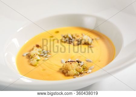 Pumpkin soup in white bowl. Served main course close up. Vegetable cream soup decorated with seeds. Restaurant food portion, main course. Vegetarian supper. Dinner, gourmet meal in plate