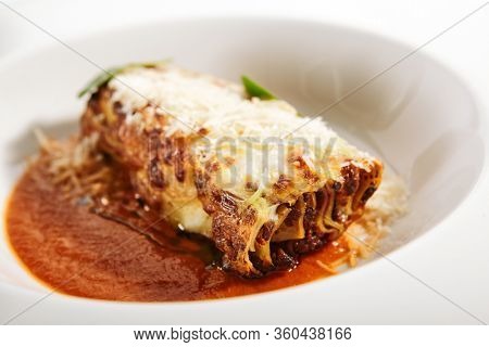 Lasagna bolognese close up. Served traditional Italian cuisine. DIsh with pasta, meat, tomato sauce, grated cheese and basil leaves in plate. Italy culinary. Restaurant food portion, main course