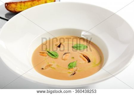 Chilean mussels soup in white bowl. Served main course close up. Seafood cream soup with roasted bread slice. Restaurant food portion, main course with toast. Dinner, gourmet meal in plate