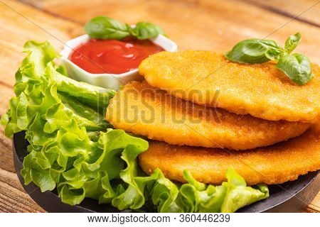 Breaded Chicken Breasts, Schnitzel And Ketchup Sauce On Black Burned On Wooden Background Close Up.