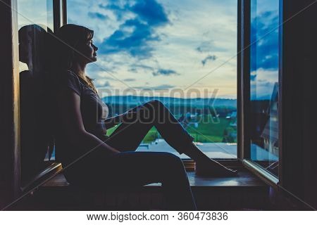 Silhouette Of Young Woman Sitting On A Window And Looking On A Beautiful Mountain View