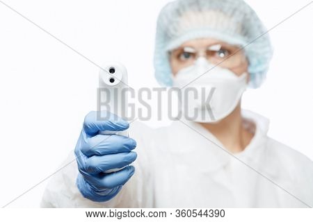 Close-up shot of doctor wearing protective suit abd surgical mask using infrared forehead thermometer (thermometer gun) to check body temperature for virus symptoms - coronavirus outbreak concept