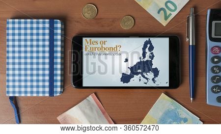 Covid-19 Economic Crisis: A Smartphone With A Question About Mes Or Eurobond On A Wooden Desk With S