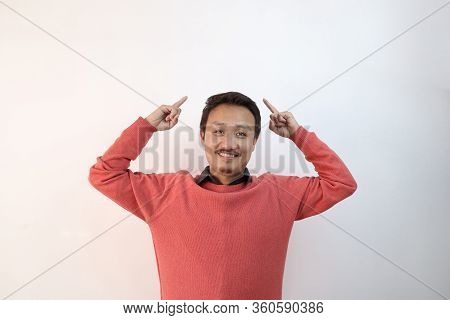 A Man In Pink Sweater Isolated In White Background Pointing Fingers Towards A Blank Copy Space Area