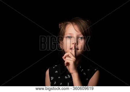 Sign Of The Tsss, Secret And Silence. A Little Girl 6 Years Old, Against A Dark Background. Emotiona