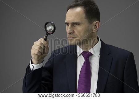 Concentrated Male Adult Ceo In Formal Suit, Tie Looking Through Magnifier, Isolated Grey Background.