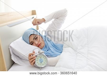 Oversleeping Asian Muslim Woman Wearing White Sleepwear Lying On Bed, Missing Ring Of Alarm Clock Wa