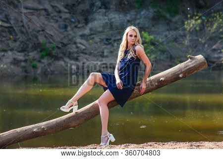 Young Beautiful Blond Woman In Blue Mini Dress And Floral Wreath Standing And Trying Water On Summer