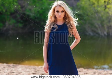 Young Beautiful Blond Woman In Blue Mini Dress And Floral Wreath Standing And Trying Water On Summer