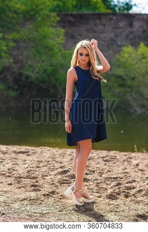 Young Beautiful Blond Woman In Blue Mini Dress And Floral Wreath Standing And Trying Water On Summer
