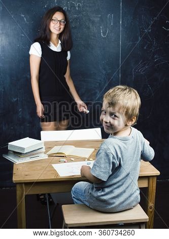 Little Cute Boy In Glasses With Young Real Teacher, Classroom Studying At Blackboard School Kido