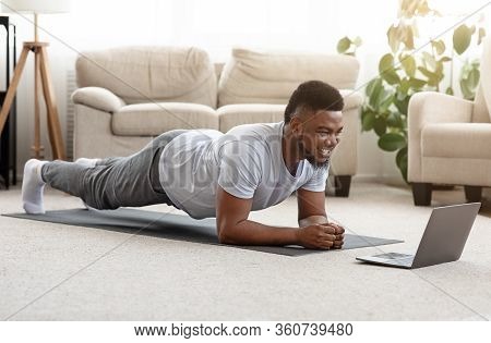Training At Home. Sporty Man Doing Yoga Plank While Watching Online Tutorial On Laptop, Exercising I