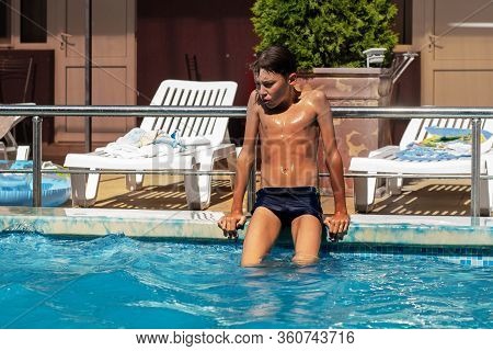 A Sad Lonely Boy Sits On Board A Swimming Pool And Is Bored. The Concept Of Loneliness And Depressio
