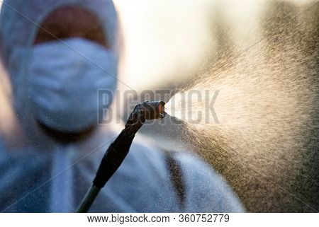 Man in protective equipment decontaminating and spraying on a public place as a prevention against Coronavirus disease 2019, COVID-19. Coronavirus pandemic.