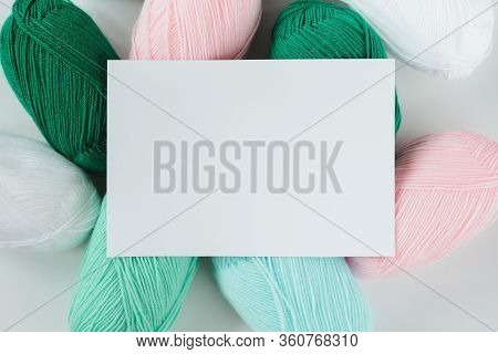 White Paper Sheet On Acrylic Soft Pastel Colored Wool Yarn Thread Skeins Heap On White Background, T