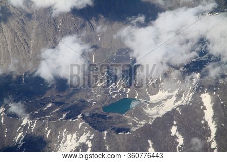 Cenic Mountains View From The Plane. Beautiful Top Landscape. Mountains Surrounded By Clouds. Ice An